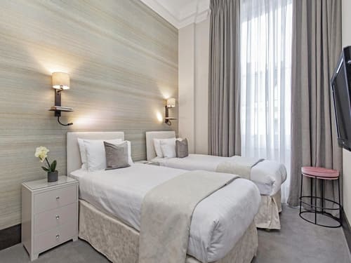 130 Queensgate, Kensington: Twin beds against a textured wall with sconce lights