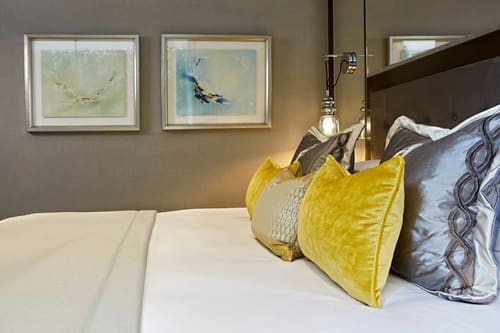 Cheval Hyde Park Gate, Kensington: Bed with yellow velvet cushions and artwork