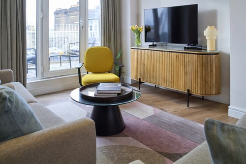 Cheval Harrington Court, Kensington: Living room with yellow chair and TV sideboard
