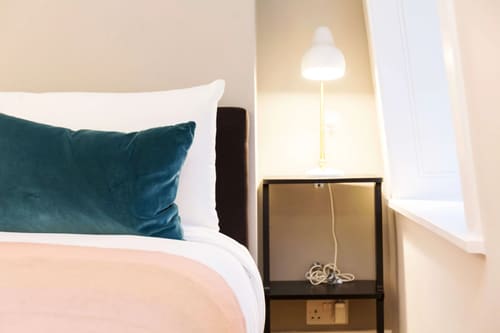 The Bank Apartments, East London: Bed with teal cushion and bedside lamp