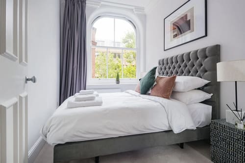 The Sloane Gardens Apartments, Chelsea: Bedroom with grey buttoned headboard and arched window