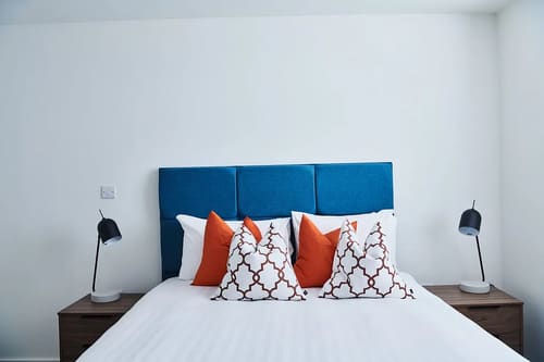The Shoreditch Warehouse Apartments, East London: Bed with blue headboard and orange cushions