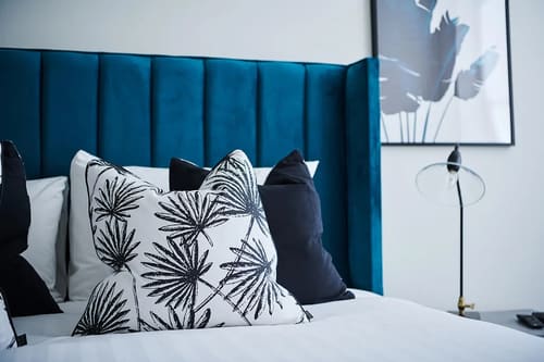 The Shoreditch Warehouse Apartments, East London: Bed with blue velvet headboard and palm-print cushion
