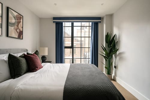 The Spitalfields Urban Rest Apartments, East London: Bed with grey throw by tall window